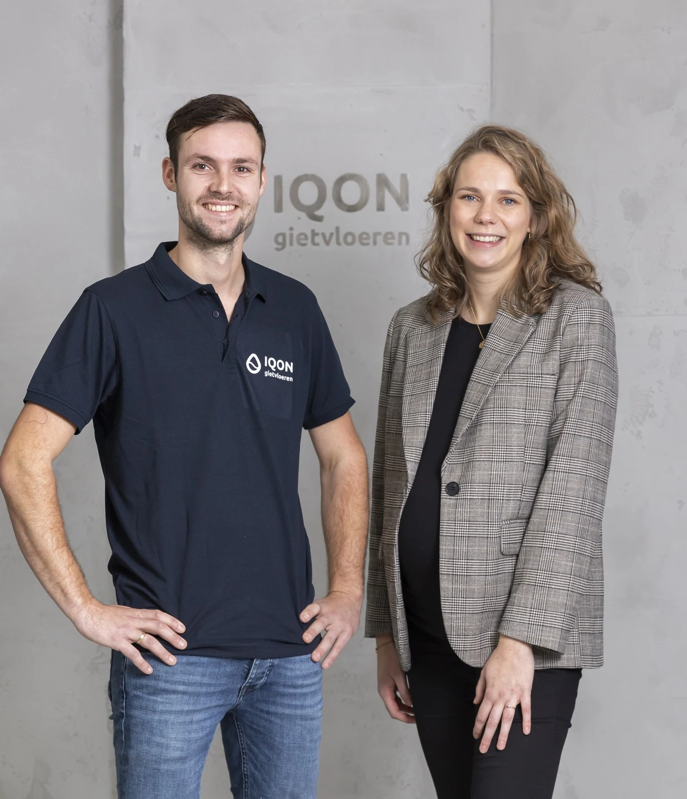 Twee medewerkers van IQON Gietvloeren voor de betonnen wand met het logo