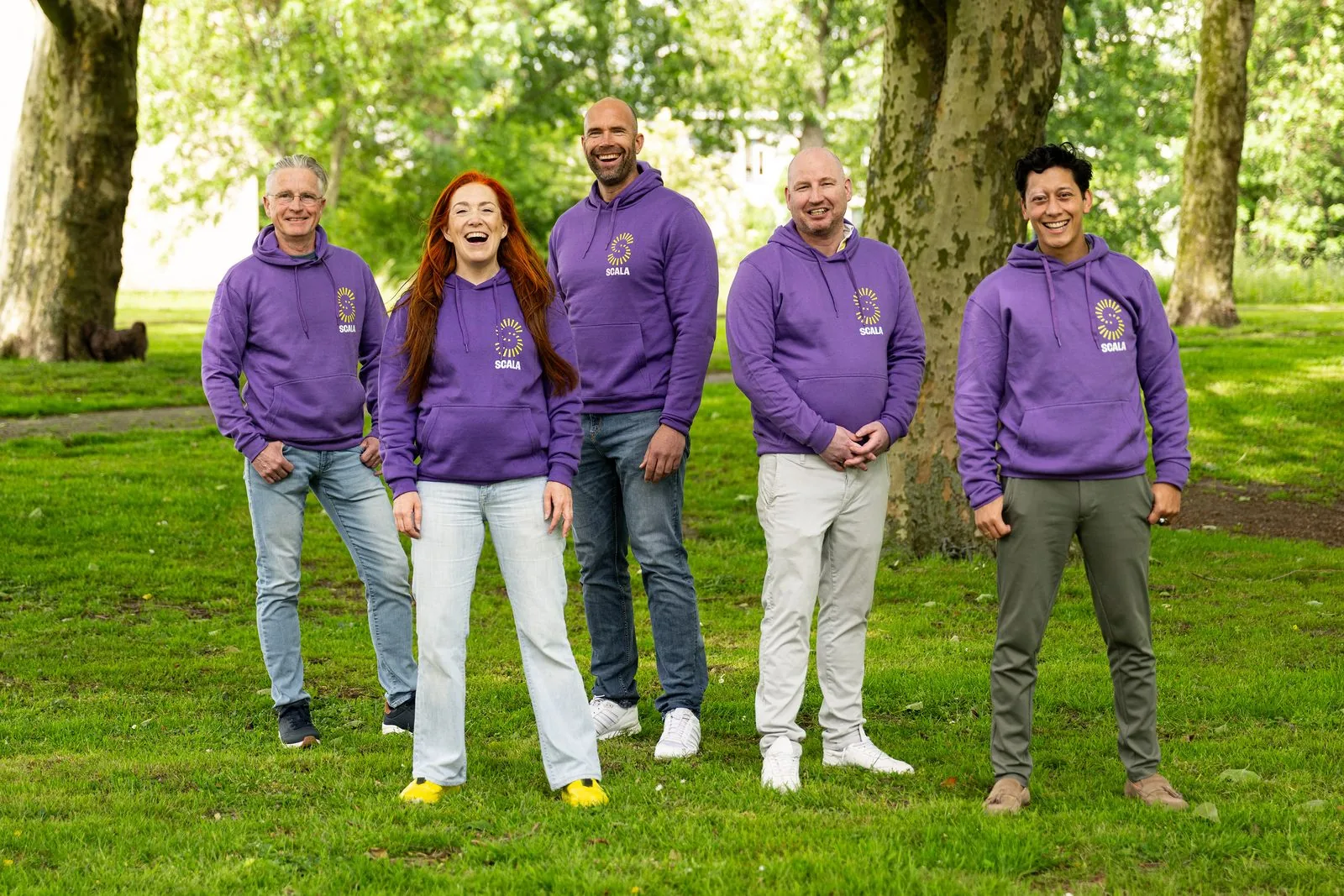 Vijf mensen in paarse Scala-hoodies in een park